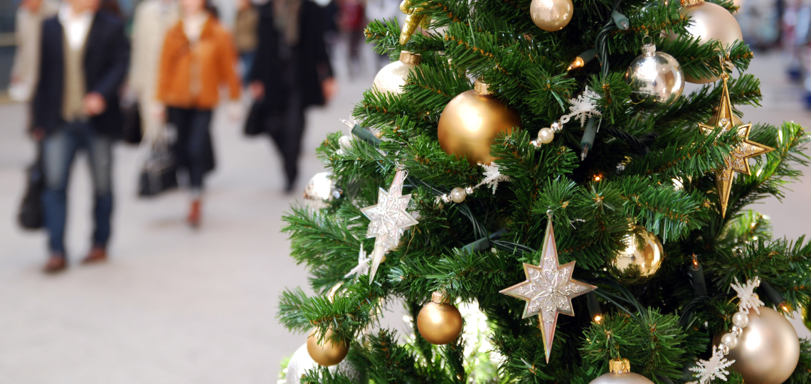 Imagen de un árbol de Navidad junto a personas realizando compras